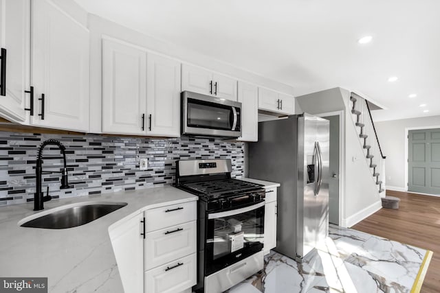 kitchen with appliances with stainless steel finishes, tasteful backsplash, white cabinetry, sink, and light stone counters