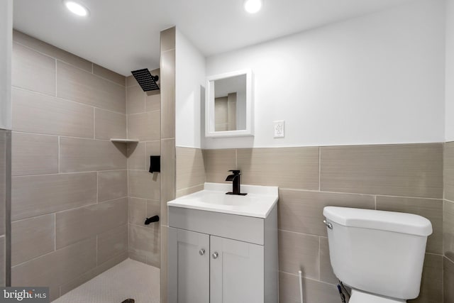 bathroom with vanity, toilet, tile walls, and a tile shower