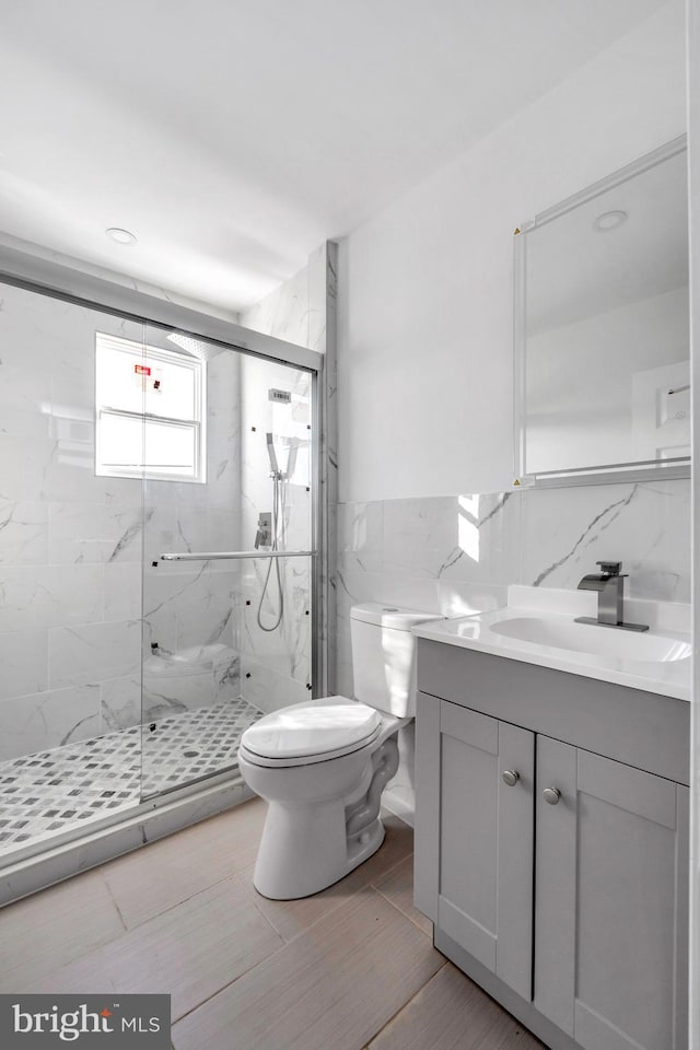 bathroom featuring vanity, toilet, an enclosed shower, and tile walls