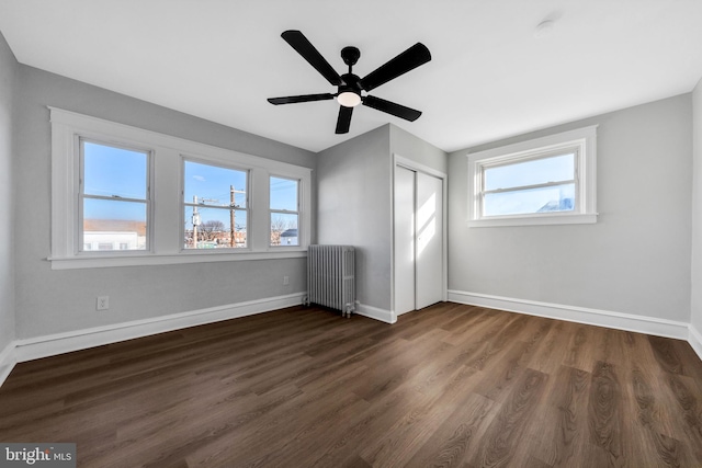 unfurnished bedroom featuring ceiling fan, radiator, dark hardwood / wood-style floors, and a closet