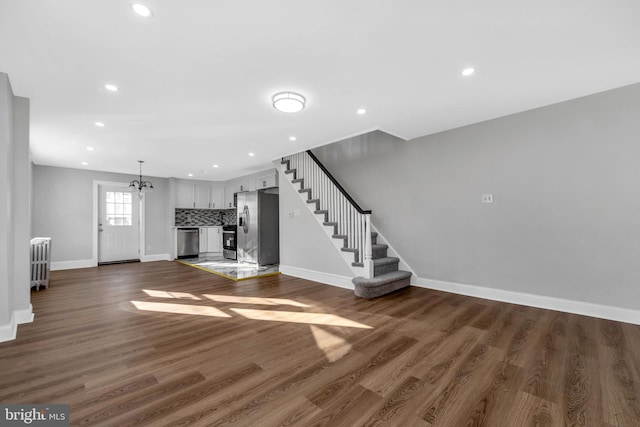 unfurnished living room with dark hardwood / wood-style flooring, radiator, and an inviting chandelier