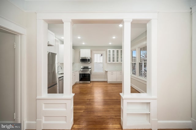 kitchen featuring sink, appliances with stainless steel finishes, hardwood / wood-style floors, decorative columns, and white cabinets