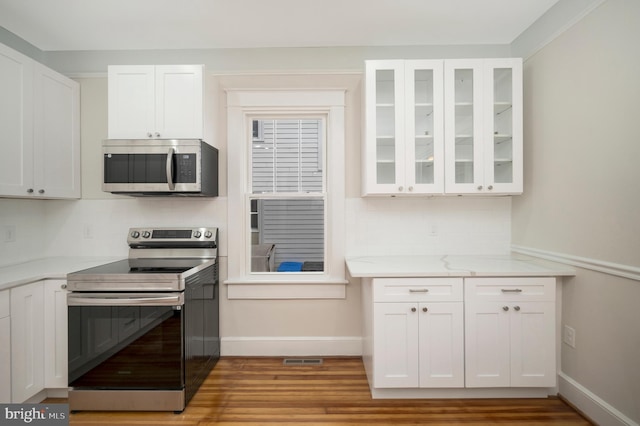 kitchen featuring white cabinetry, appliances with stainless steel finishes, light hardwood / wood-style floors, and decorative backsplash