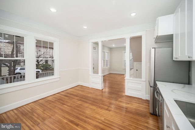 unfurnished dining area featuring decorative columns, plenty of natural light, and light hardwood / wood-style floors