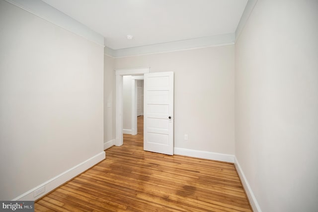 empty room with hardwood / wood-style flooring and crown molding