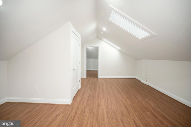 additional living space with light hardwood / wood-style flooring and lofted ceiling with skylight