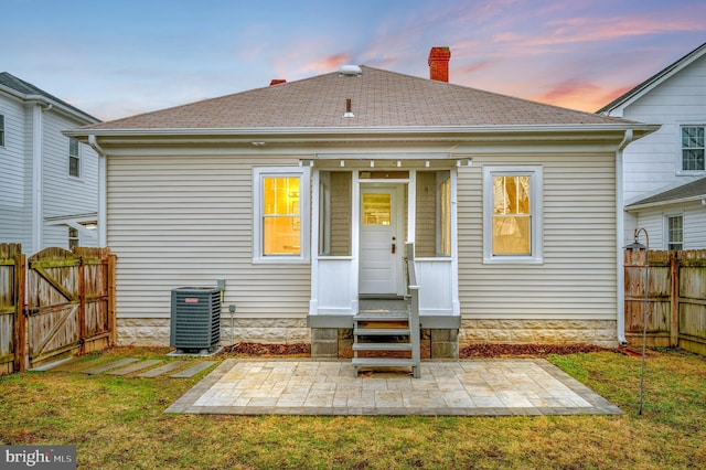 back house at dusk featuring cooling unit, a yard, and a patio area