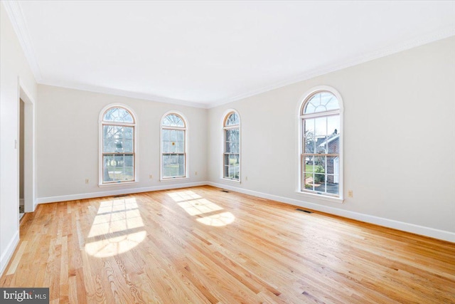 empty room with ornamental molding, baseboards, visible vents, and light wood finished floors