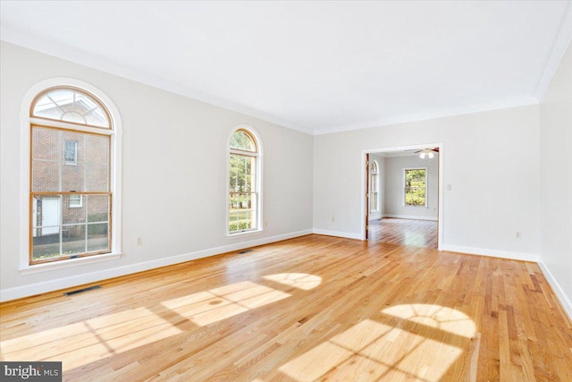 spare room featuring light wood-style flooring, visible vents, baseboards, and ornamental molding