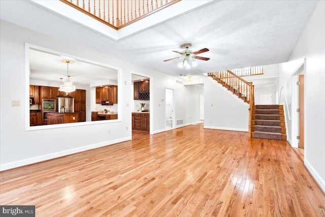 unfurnished living room featuring stairs, visible vents, light wood-style floors, baseboards, and ceiling fan with notable chandelier