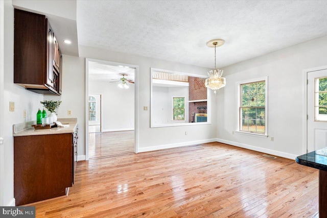 unfurnished dining area with visible vents, baseboards, a textured ceiling, and light wood finished floors