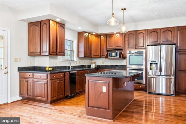 kitchen with a center island, brown cabinets, appliances with stainless steel finishes, dark stone countertops, and light wood-type flooring