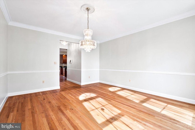 unfurnished room featuring baseboards, ornamental molding, wood finished floors, and a notable chandelier