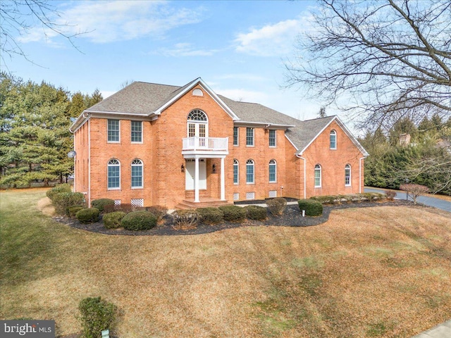 colonial house with a balcony, a front yard, and brick siding