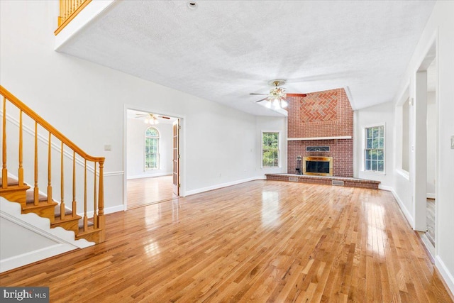 unfurnished living room with a healthy amount of sunlight, a brick fireplace, light wood-style flooring, and stairway