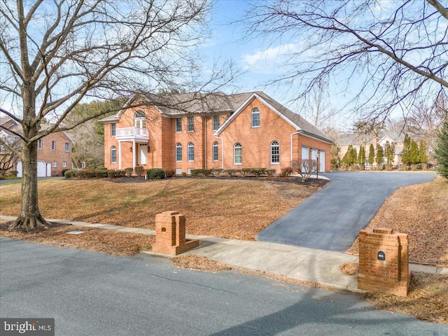 colonial home featuring a garage, aphalt driveway, a front yard, and brick siding