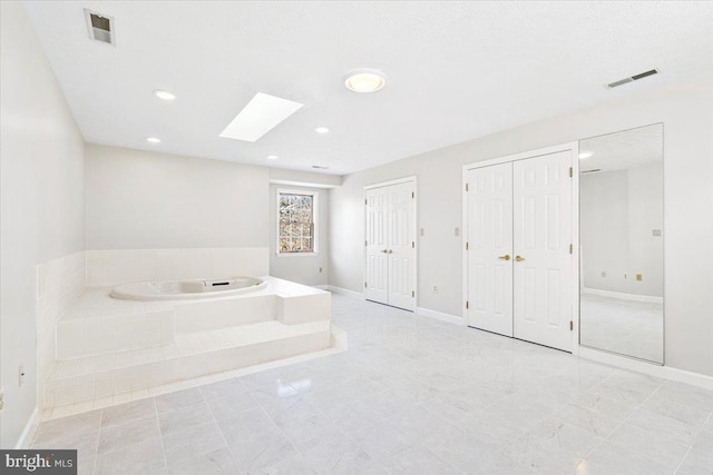 bathroom featuring a garden tub, baseboards, a skylight, and visible vents