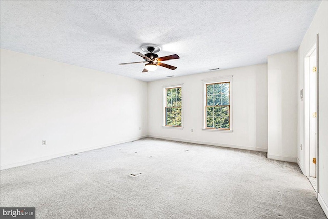 spare room with light carpet, a textured ceiling, baseboards, and a ceiling fan