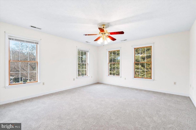 carpeted empty room featuring a textured ceiling, ceiling fan, visible vents, and baseboards