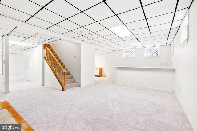 below grade area with stairs, a drop ceiling, baseboards, and light colored carpet