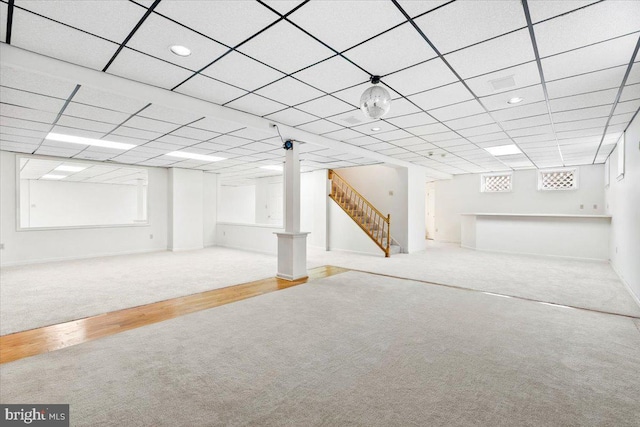 below grade area featuring carpet floors, wood finished floors, a drop ceiling, baseboards, and stairs