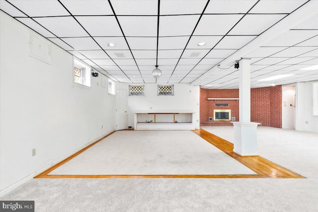 below grade area featuring baseboards, a drop ceiling, carpet, and a brick fireplace