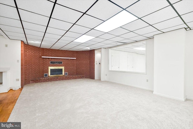 unfurnished living room featuring a paneled ceiling, brick wall, a fireplace, and light colored carpet