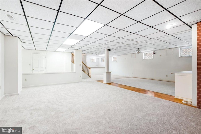 below grade area with a paneled ceiling, light wood finished floors, stairs, and light colored carpet