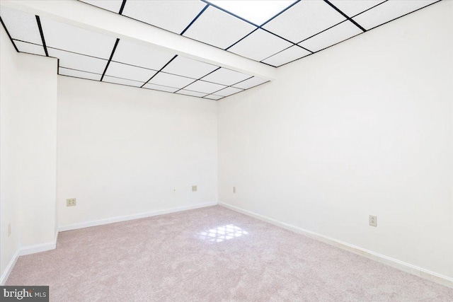 spare room featuring baseboards, a drop ceiling, and light colored carpet