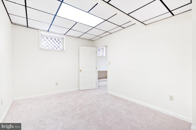 unfurnished room featuring a paneled ceiling, light colored carpet, and baseboards