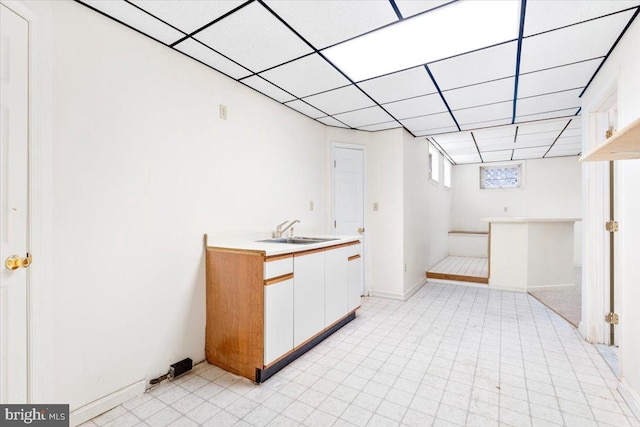 interior space featuring a drop ceiling, a sink, and baseboards