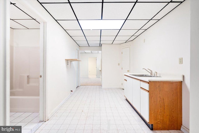 interior space with baseboards, light countertops, a paneled ceiling, white cabinetry, and a sink