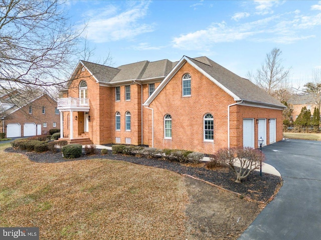 view of front of property with aphalt driveway, a balcony, a garage, brick siding, and a front lawn