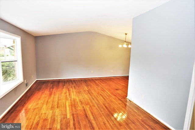 empty room featuring hardwood / wood-style flooring, a chandelier, and vaulted ceiling