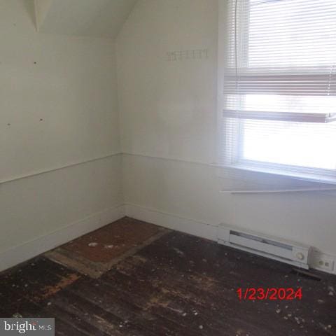 empty room with lofted ceiling, hardwood / wood-style floors, and a baseboard radiator