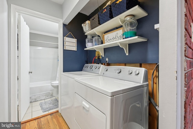 clothes washing area with washing machine and dryer and light wood-type flooring