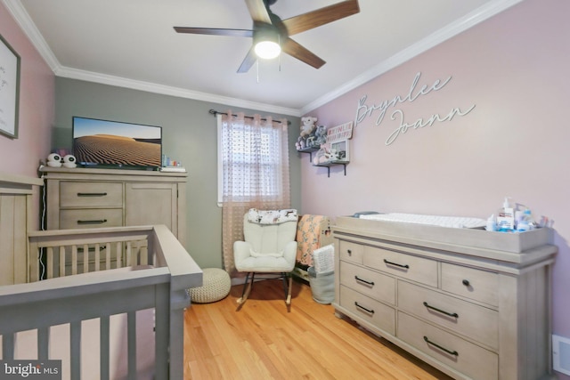 bedroom featuring crown molding, a crib, ceiling fan, and light wood-type flooring