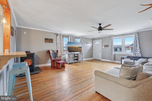 living room featuring hardwood / wood-style flooring, ceiling fan, ornamental molding, and a wood stove