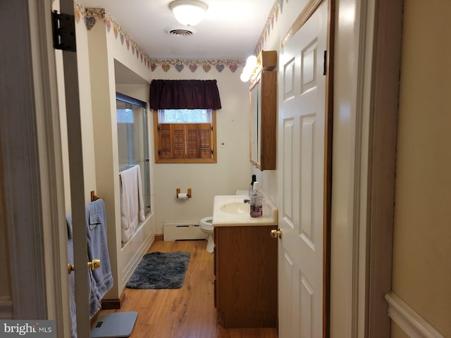 full bathroom with bath / shower combo with glass door, wood-type flooring, a baseboard radiator, vanity, and toilet