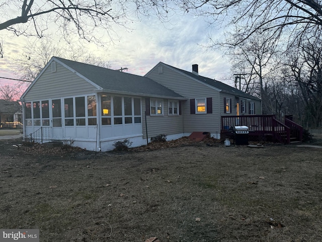 property exterior at dusk featuring a wooden deck, a sunroom, and a lawn