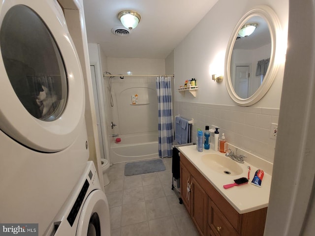 full bathroom featuring shower / tub combo with curtain, tile walls, vanity, stacked washer / drying machine, and toilet