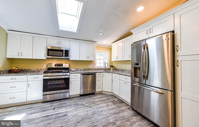 kitchen with white cabinetry, appliances with stainless steel finishes, light hardwood / wood-style floors, and dark stone countertops