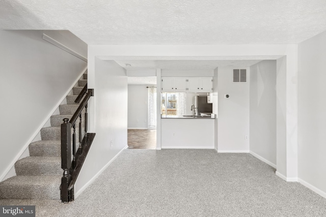 interior space featuring visible vents, stairs, a textured ceiling, carpet floors, and a sink