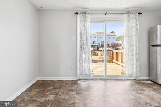 empty room featuring a textured ceiling, stone finish floor, and baseboards