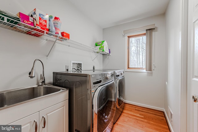 washroom featuring sink, washer and clothes dryer, light hardwood / wood-style floors, and cabinets