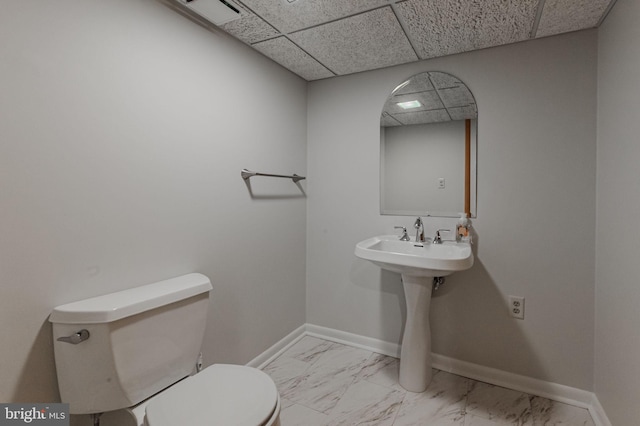 bathroom with a paneled ceiling, toilet, and sink