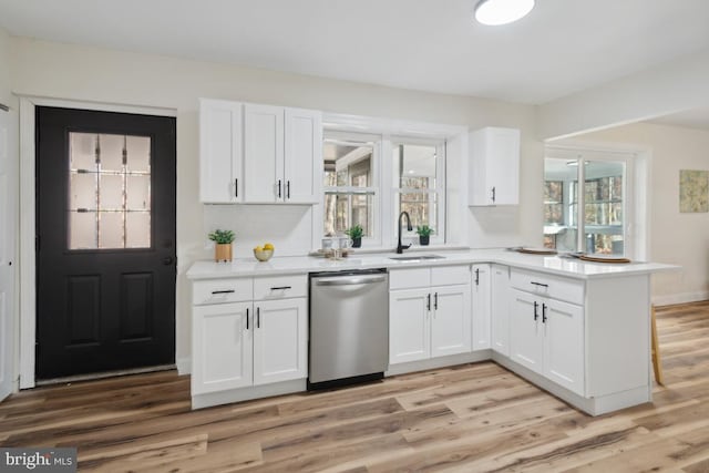 kitchen featuring light wood-style flooring, a peninsula, a sink, white cabinets, and dishwasher