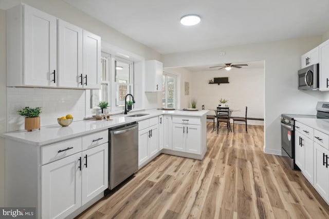 kitchen with stainless steel appliances, a sink, white cabinetry, light wood-type flooring, and decorative backsplash