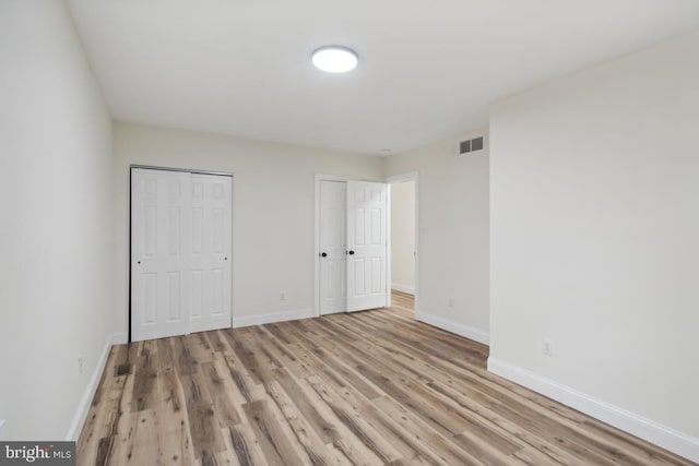 unfurnished bedroom featuring multiple closets, visible vents, light wood-style floors, and baseboards