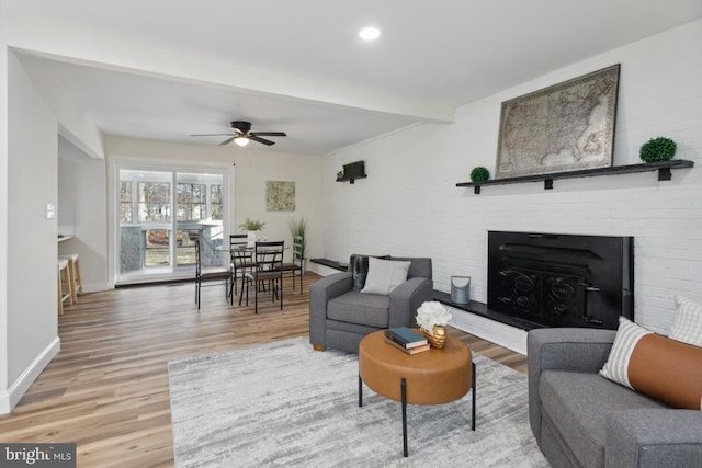 living area with light wood finished floors, a fireplace with raised hearth, a ceiling fan, beamed ceiling, and baseboards